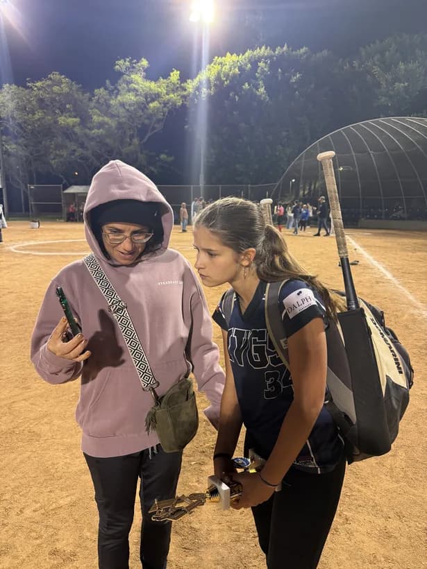 My wife and daughter under the lights at a softball game, looking at a phone together.